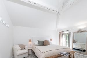 a white bedroom with a bed and a chair at La Bâtisse en Blanc in Golfe-Juan