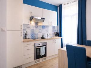 a kitchen with white cabinets and a blue wall at Le Spacieux à Saint-Omer - 2 chambres, centre et gare à pied, parking privé gratuit in Saint-Omer
