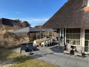 a patio with a table and chairs and umbrellas at Luxe Duinvilla Stern met sauna voor 8 personen nabij strand en dorp Nes in Buren