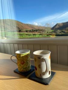 two coffee cups sitting on a table in front of a window at 49 Erw Porthor in Tywyn