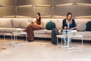 two women sitting on a couch looking at their phones at SuMa Recoleta Hotel in Buenos Aires