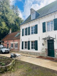 a white house with green shutters and a dog in front of it at Maison de caractère au calme en pleine campagne in Rollancourt