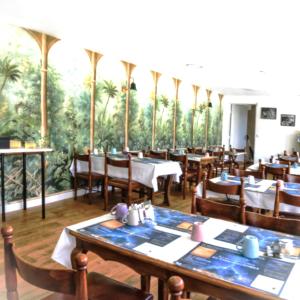 a restaurant with tables and chairs and palm trees at Hotel La Baie Royale in Pontorson