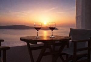 two glasses of wine sitting on a wooden table with the sunset at Yposkafo Suites - Studio - Santorini in Fira +17 photos