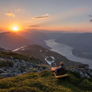 a man sitting on a hill watching the sunset at Affordable Luxury Apt - Hotel Vibe - Heart of Voss in Vossevangen