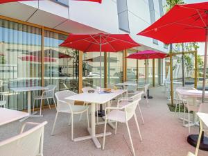 a restaurant with tables and chairs with red umbrellas at ibis Styles Salon de Provence in Salon-de-Provence
