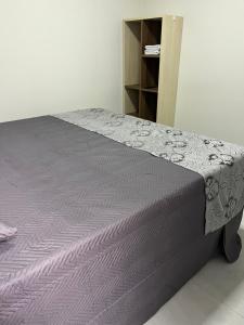 a bed with a purple bedspread and a book shelf at Residenc Mazonetto in Primavera do Leste