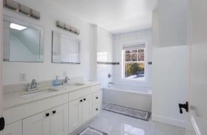 a white bathroom with two sinks and a tub and a window at Charming Home for a Perfect Escape in East Hampton +27 photos