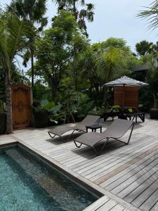 a deck with two chairs and an umbrella next to a pool at Koji Collection in Kerobokan +16 photos
