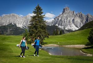 two women standing on a golf course in front of a mountain at Hotel Sassongher - Preferred Hotels & Resorts in Corvara in Badia