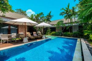 a pool with chairs and umbrellas next to a house at Kejora Beachfront Villas in Sanur