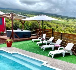a group of chairs and an umbrella next to a pool at Villa Le Cyprès classée 4 Etoiles billard, piscine et jacuzzi in Saint-Joseph