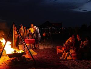a group of people standing around a fire at night at Lantern Luxury Camp in Merzouga