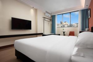 a bedroom with a white bed and a flat screen tv at 花祺巨幕影院酒店 儋州那大镇夏日广场汽车站店 in Danzhou
