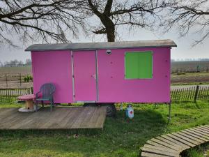 a pink house with a chair and a table at Pipowagen Doe Maar Roze in Bant +6 photos