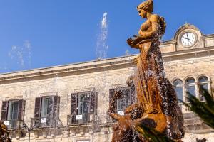 a fountain in front of a building with a clock at Archimede Charm B&B - Historical Palace in Ortigia in Syracuse