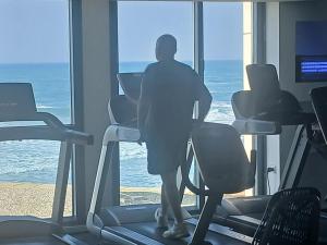 a man on a treadmill in a gym looking out the window at מרינה טוורס מלון בוטיק in Herzliya B