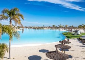 a swimming pool with straw umbrellas on a beach at Nieuw Casa Santa Rosalia uitzicht op zwembad in Torre-Pacheco