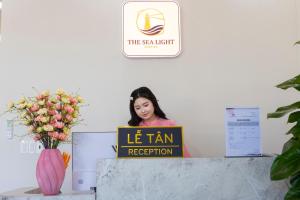 a woman is sitting at a desk with a sign at The Sea Light Hotel Phú Quốc- Sunset and Ocean View in Phú Quốc