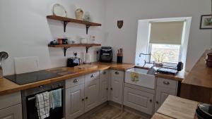 a kitchen with white cabinets and a sink and a window at Rose Cottage Solway Self Catering in Cardurnock