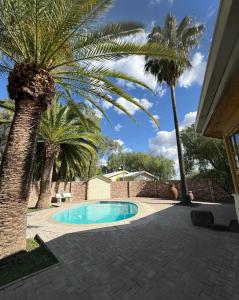 a swimming pool with palm trees next to a house at East Gate Rest Camp in Buitepos