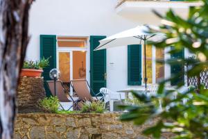 a house with green shutters and a table with an umbrella at Il Golfo e La Spiaggia - A Due Passi Da Procchio in Marciana
