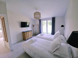 a white bedroom with two beds and a television at Gîtes Prestige LETENDART in Saint-Quentin-en-Tourmont