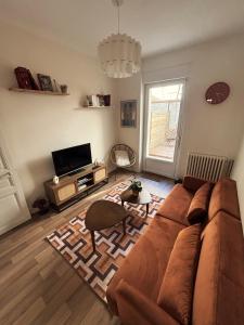 a living room with a brown couch and a tv at Le jardin secret in Reims