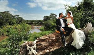 a bride and groom sitting on top of a log at Nature Lovers Camp in Sekenani