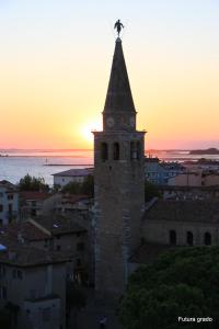 a building with a clock tower with the sunset in the background at San Pietro D'Orio Apartment in Grado +8 photos