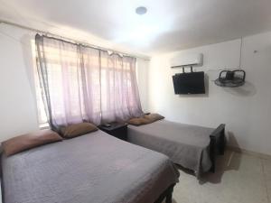 two beds in a room with a window and a tv at Casa Emilio Carranza, Linares in Linares