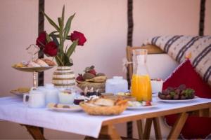 a breakfast table with food and a bottle of orange juice at Merzouga Retreat Camp in Merzouga +40 photos
