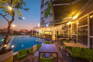 a pool with tables and chairs next to a building at Whiz Prime Hotel Hasanuddin Makassar in Makassar