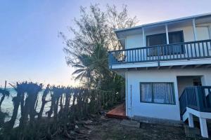 a white house with a balcony and trees at Toreaiva 91 Beachfront Studios in Arorangi