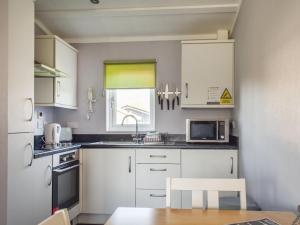 a kitchen with white cabinets and a sink and a window at Alula Lodge in Lowestoft