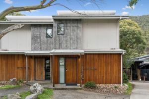 a house with wooden doors and a tree at Roses Creek Chalet B in Crackenback