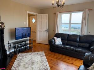 a living room with a black leather couch and a flat screen tv at Trá Leathan in Doolin