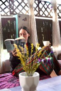 a woman sitting on a bed reading a book at Flamingos Hostel Jaipur in Jaipur