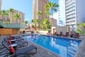 a swimming pool with chaise lounge chairs and palm trees at Ramada Plaza by Wyndham Waikiki in Honolulu