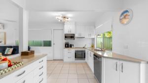 a white kitchen with white cabinets and a large window at Coastal Palms Hideaway in Bongaree