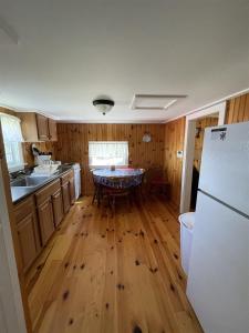 a kitchen with wooden floors and a table and a refrigerator at THE SHOPPE LIMIT 3 cabin in North Sebago