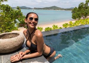 a woman in a bikini sitting next to a swimming pool at Clay Beach Samui - Beachfront Villas in Bophut