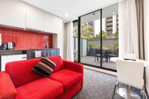 a living room with a red couch and a kitchen at Comfort Apartments Box Hill in Box Hill