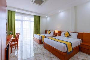 a bedroom with two beds and a desk and a window at Hanah Hotel Phan Thiet in Phan Thiet