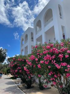 ein weißes Gebäude mit rosa Blumen davor in der Unterkunft Riad Meninx in Bin Rhilouf