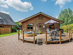a wooden cabin with a deck with a chair and an umbrella at 2 Bed in Ledbury oc-77377 in Yatton