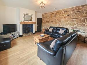a living room with a leather couch and a stone wall at 3 Bed in Morpeth oc-96236 in Amble