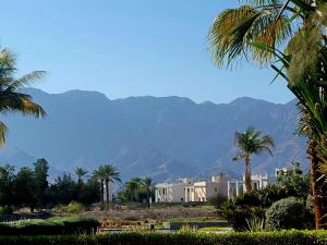 a white building with palm trees and mountains in the background at Family Floatie Flat with Pool & Workspace in As Sīfah