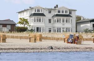 duży biały dom siedzący na plaży obok wody w obiekcie Villa Hansa am Meer w mieście Timmendorfer Strand