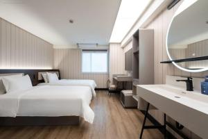 two beds in a room with a sink and a mirror at Hanting Hotel Guangzhou Tianhe in Guangzhou